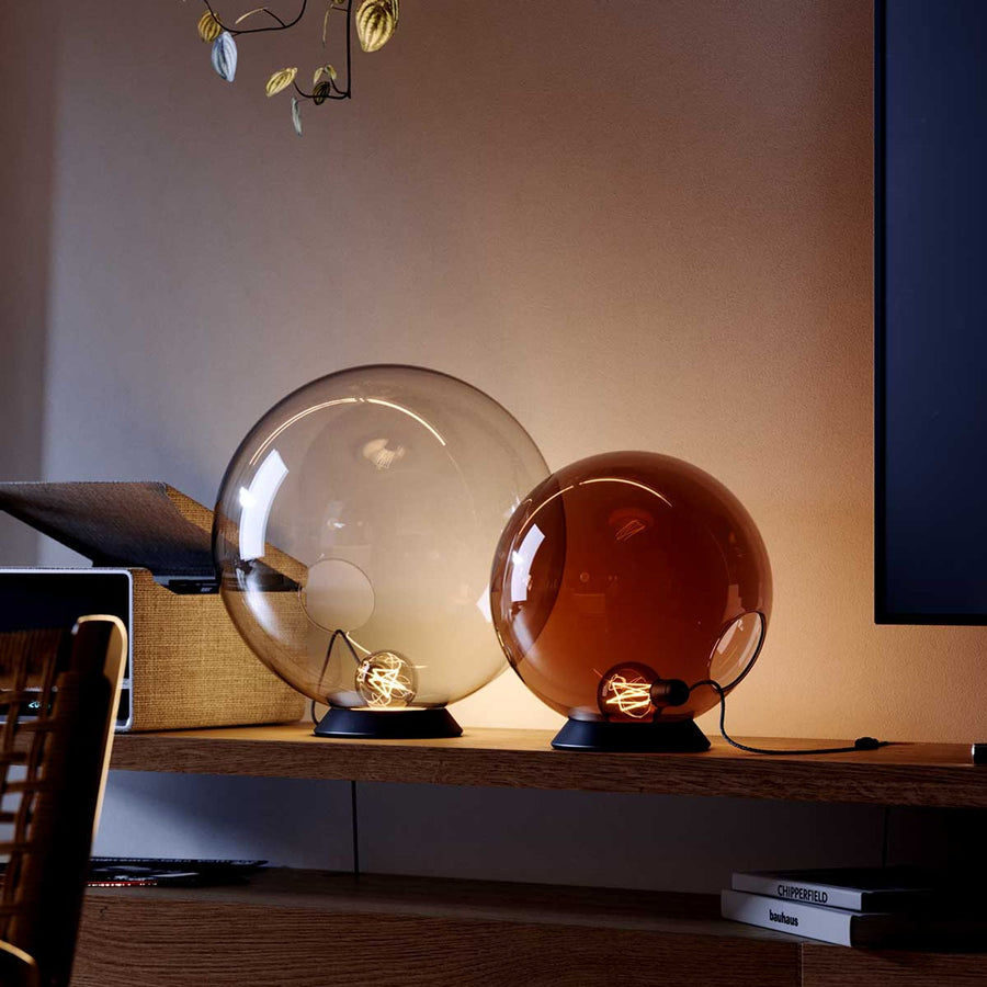 Deux globes de verre posés sur une étagère en bois, l'un transparent, l'autre ambré