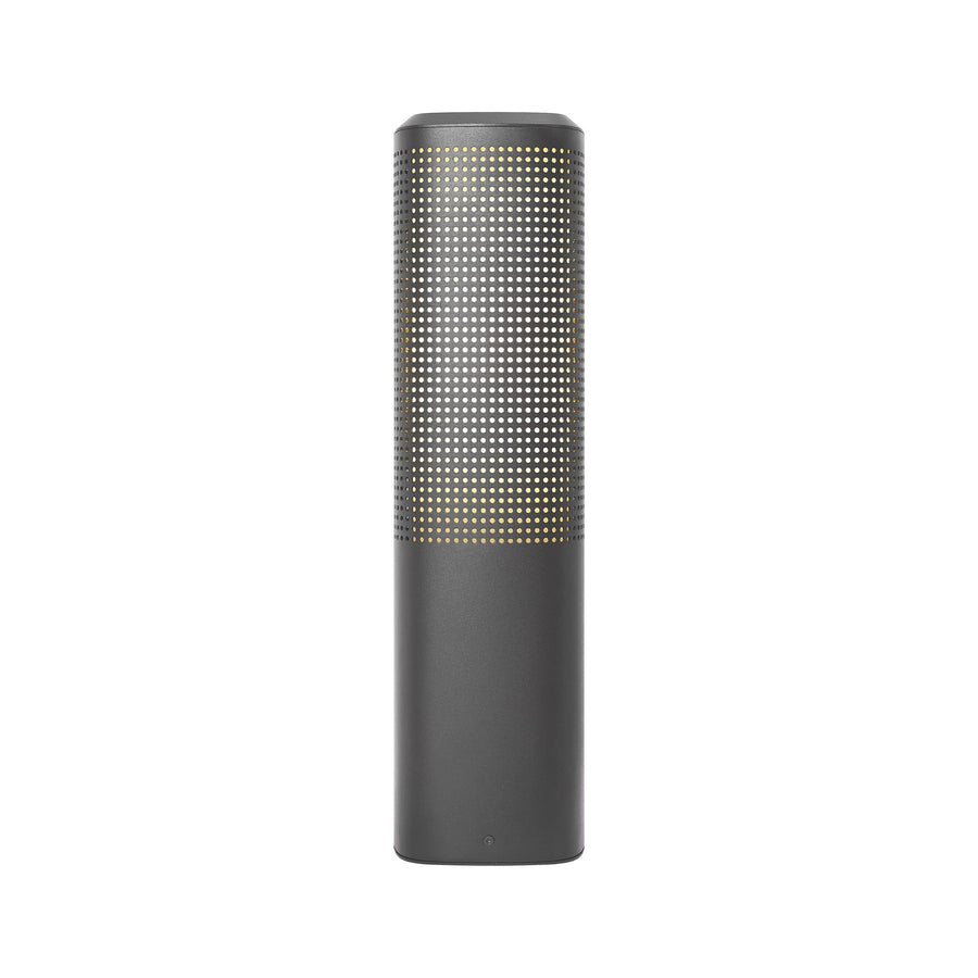 Vue de face de la borne allumée, lumière chaude filtrant par la grille métallique.