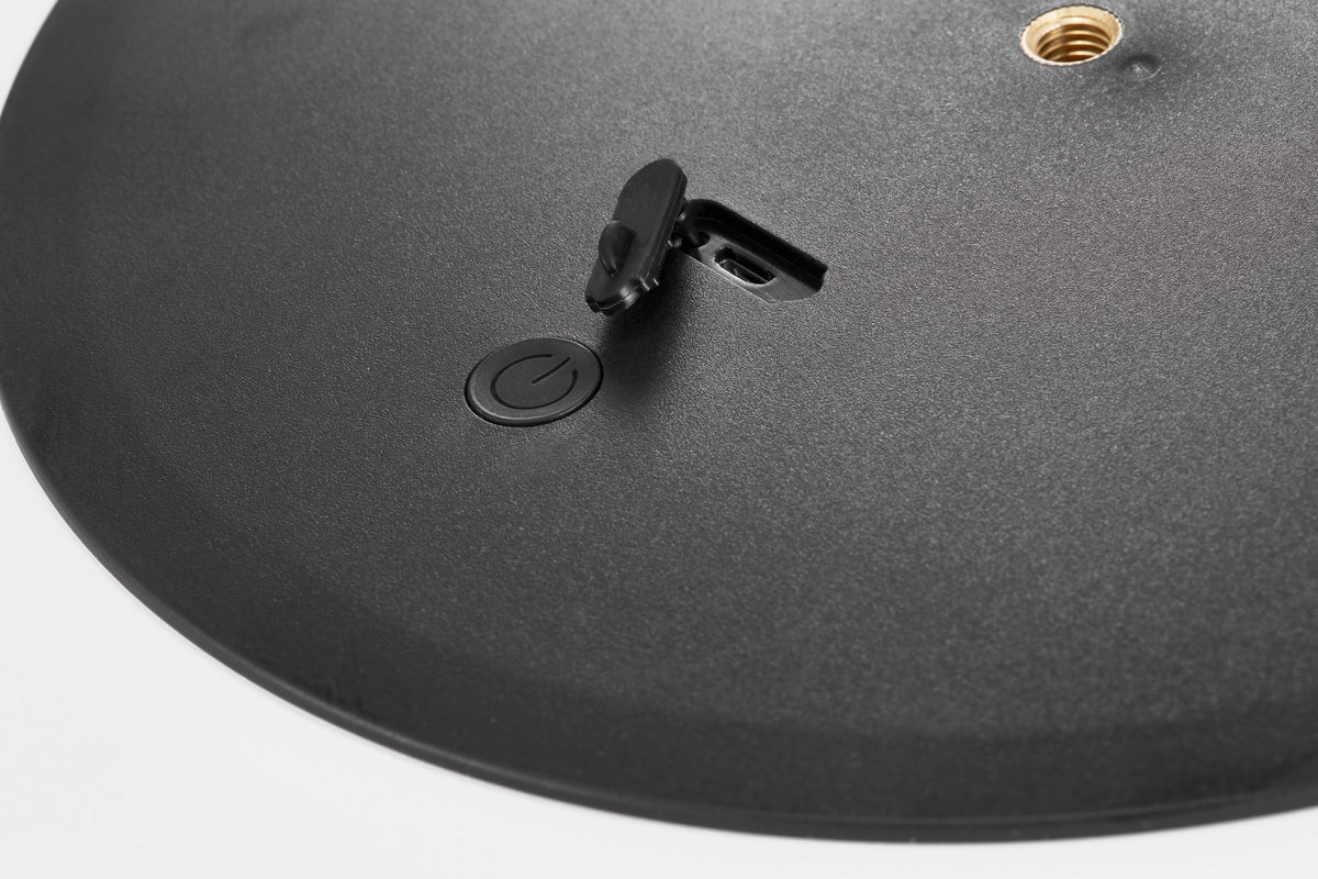 Détail du dessous noir avec bouton d'alimentation et trappe plastique près d'un filetage doré