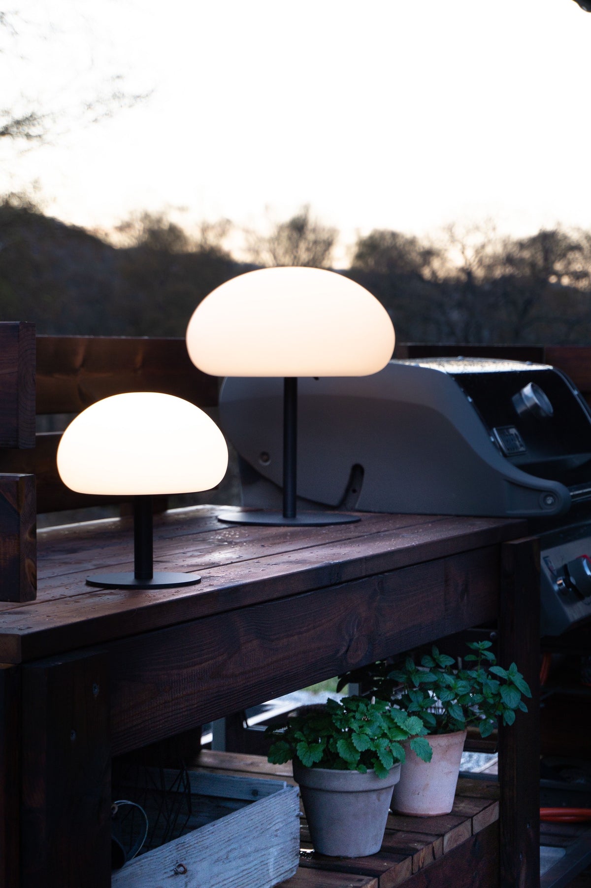 Deux lampes éclairées posées sur une table en bois près d'un barbecue.