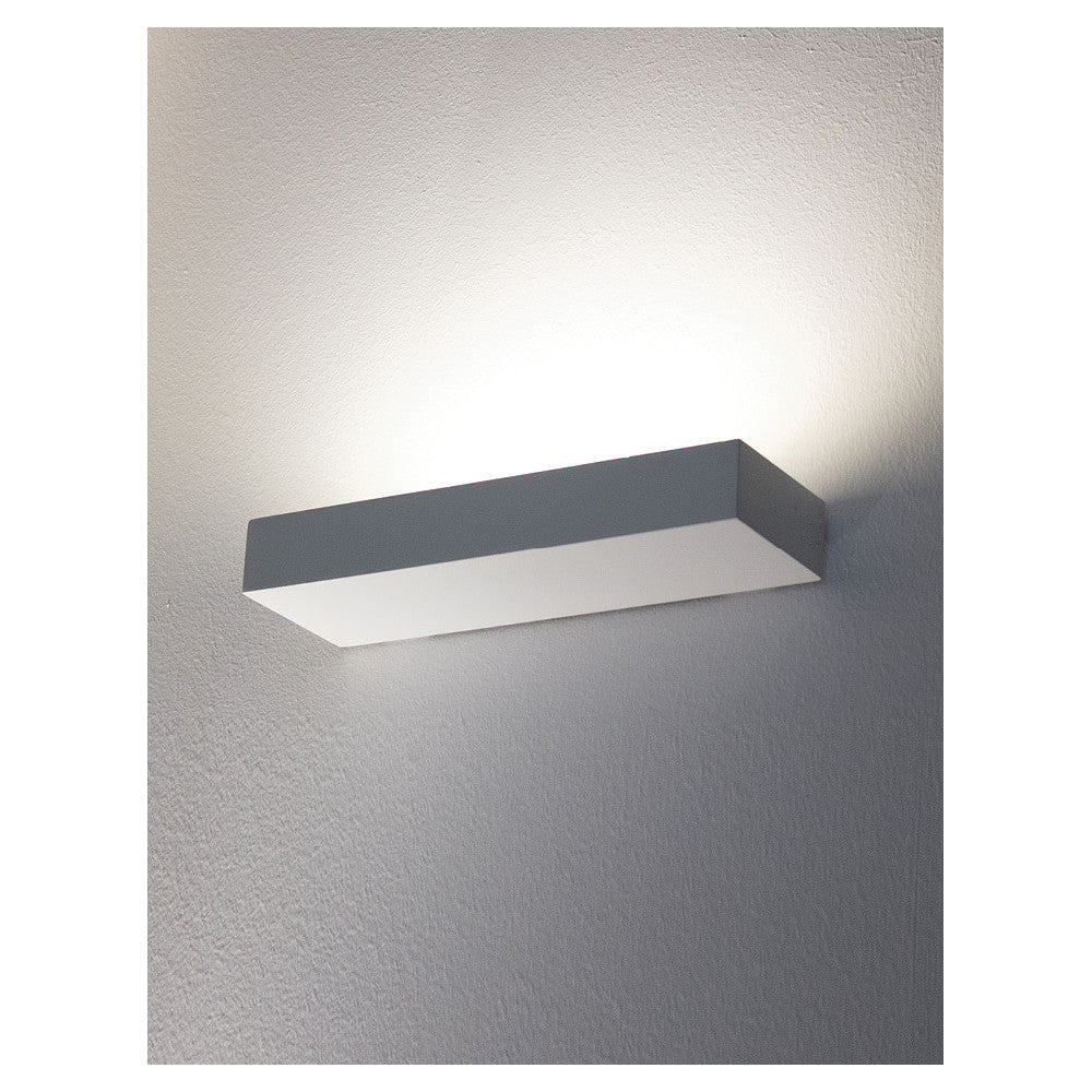 Applique fixée au mur, lumière indirecte diffusée vers le haut et le bas sur crépi gris.