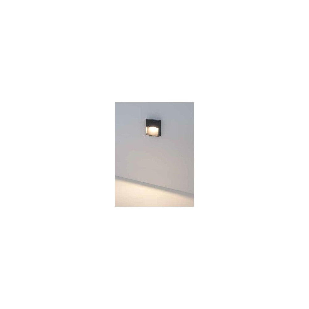 Vue d'ambiance de l'applique allumée sur mur blanc, halo lumineux diffus