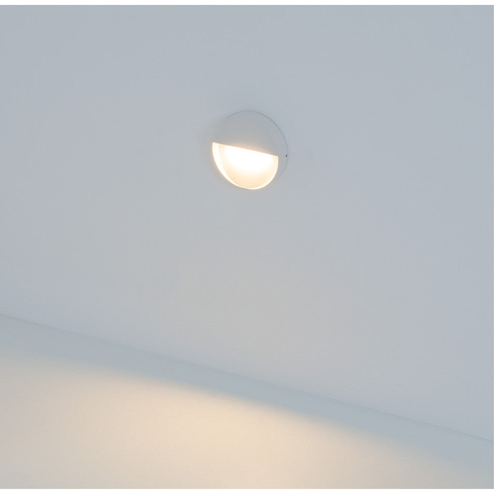 Applique murale ronde blanche installée en hauteur projetant une lumière chaude vers le bas.