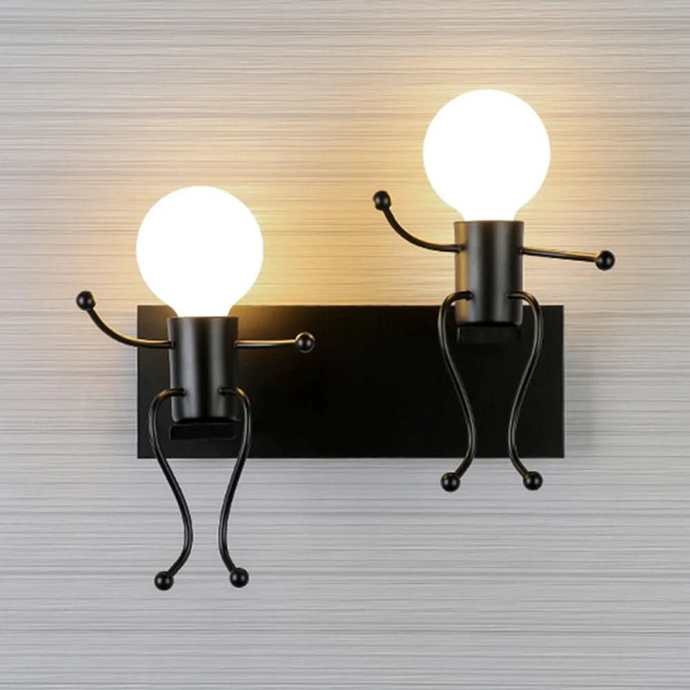 Applique noire à deux lumières allumées sur mur gris, finition métal contrastée et design ludique.
