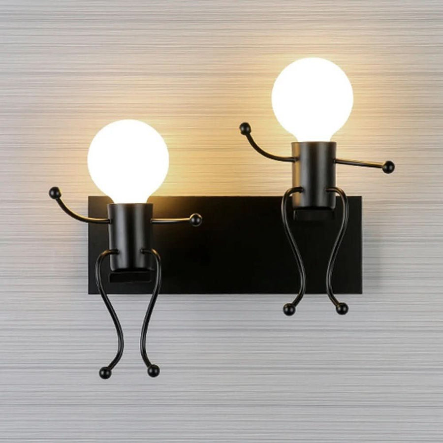 Applique noire à deux lumières allumées sur mur gris, finition métal contrastée et design ludique.