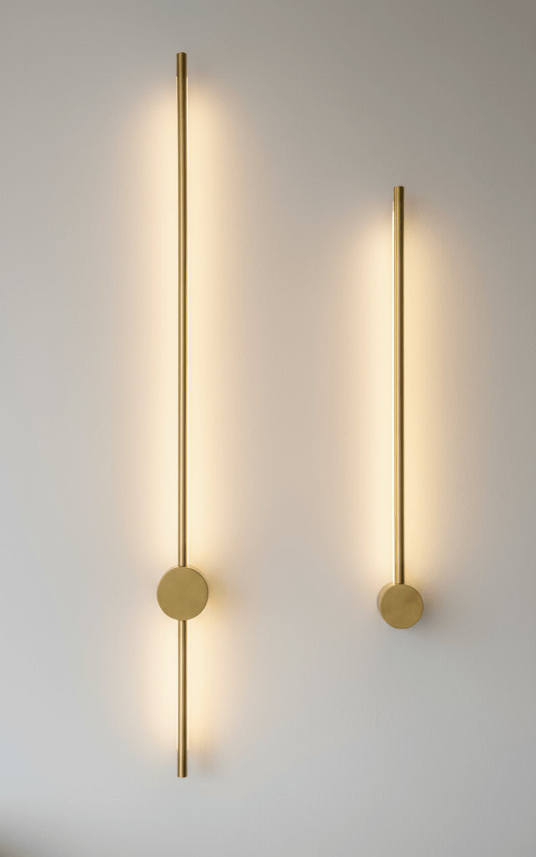 Paire d'appliques dorées allumées projetant deux halos verticaux sur mur blanc