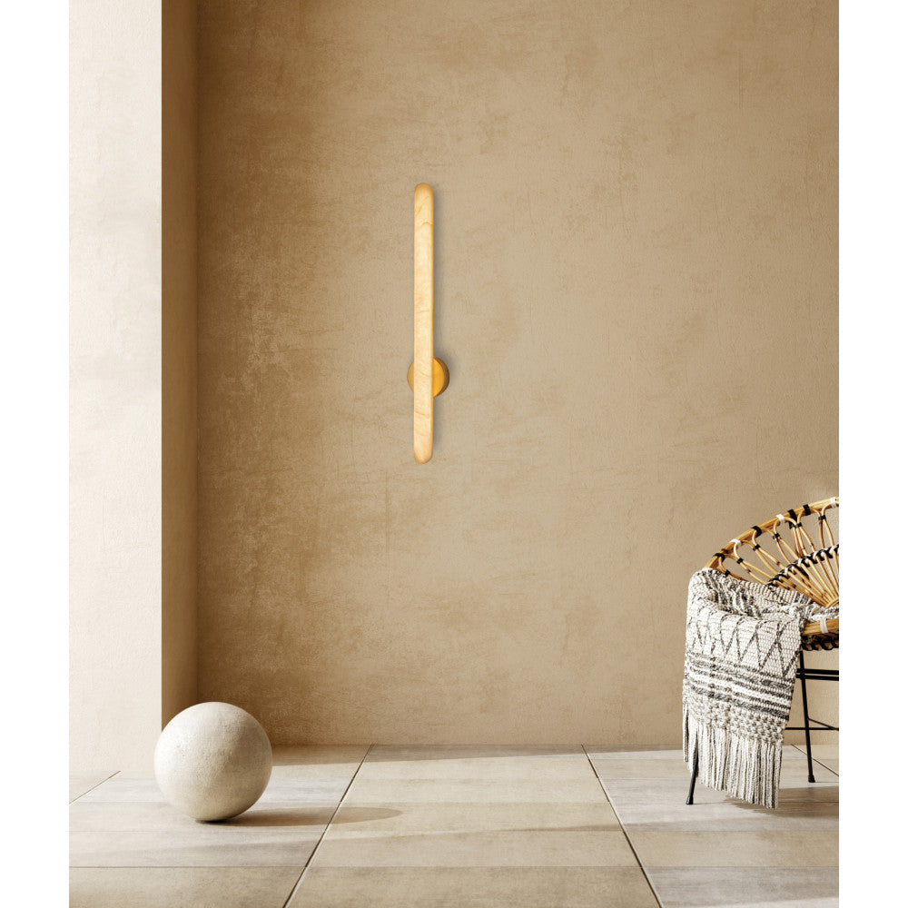 Mise en ambiance de l'applique allumée sur un mur beige, près d'un fauteuil.