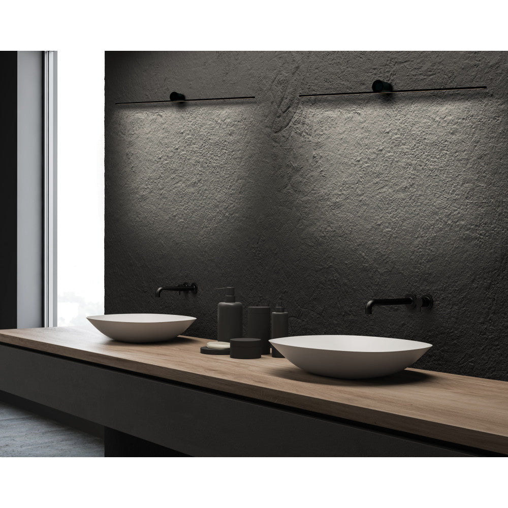 Mise en ambiance salle de bain, deux appliques noires allumées sur mur sombre texturé