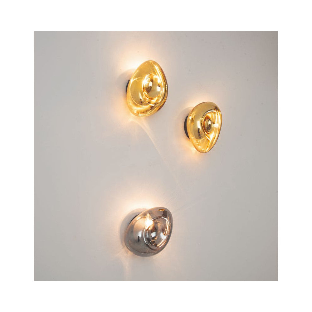 Trois appliques murales fixes sur mur blanc, deux dores et une chrome, allumees