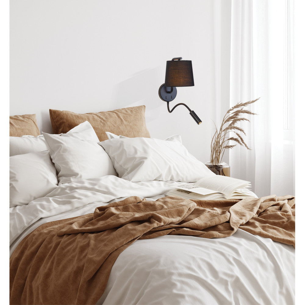 Gros plan de l'applique murale au-dessus d'un lit, linge blanc et rideau clair.