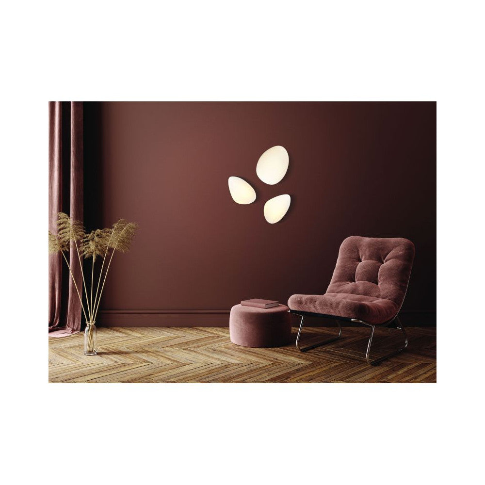 Mise en ambiance sur mur bordeaux : trois appliques ovoïdes allumées, fauteuil et plantes.