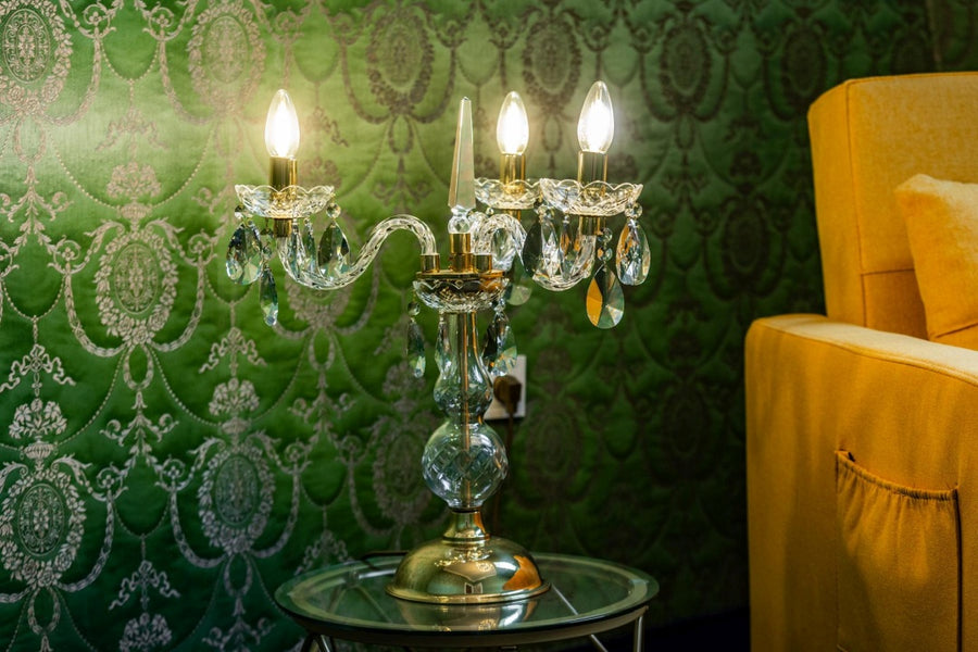 Scène d'intérieur, mur vert damassé, lampe dorée allumée posée sur guéridon.