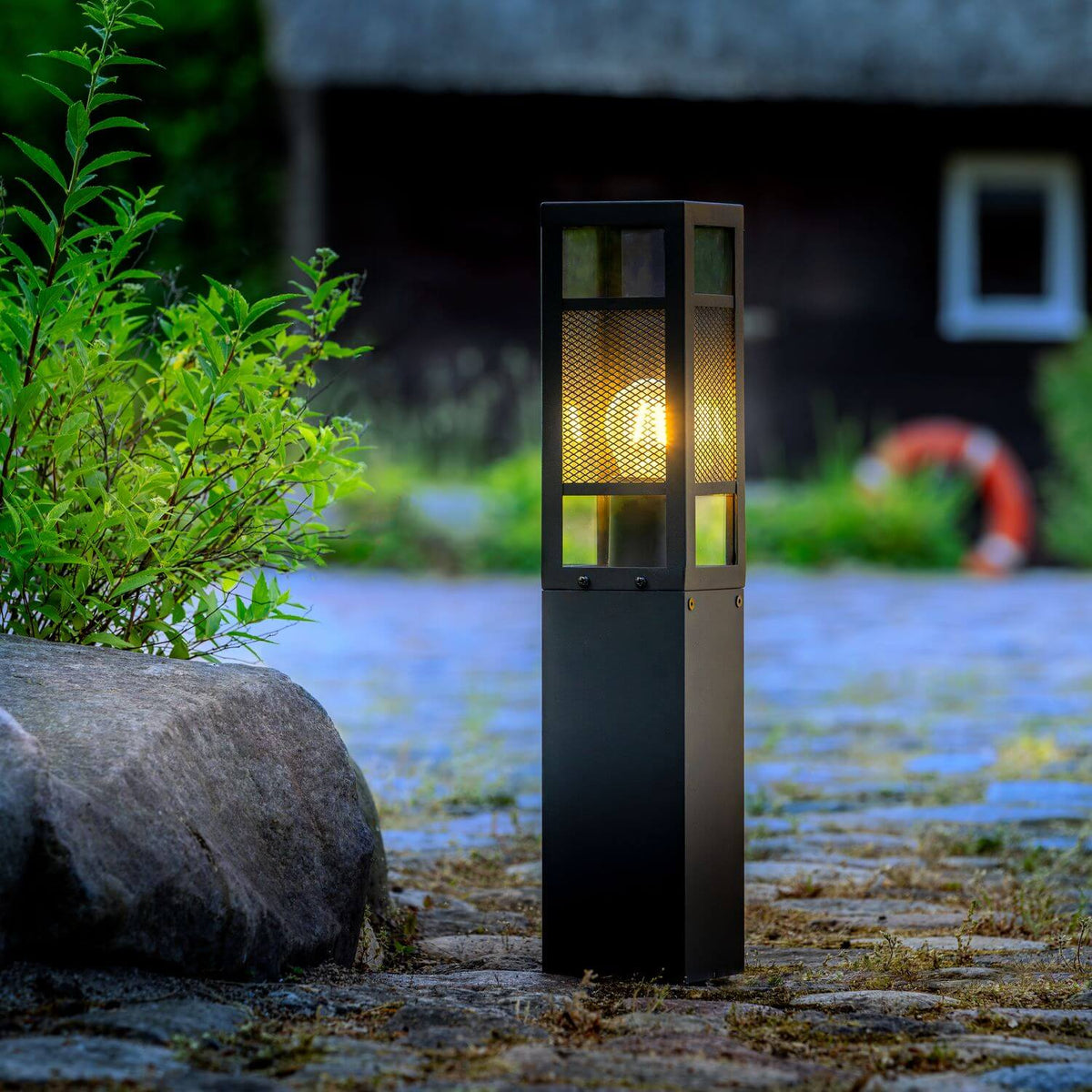 Mise en ambiance nocturne du luminaire allumé dans un jardin près d'une maison.