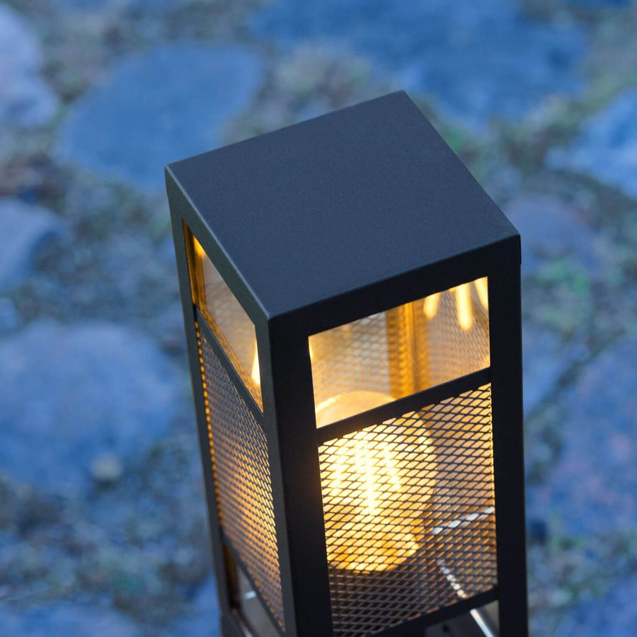 Vue rapprochée en plongée du luminaire allumé, détaillant la grille et l'ampoule.
