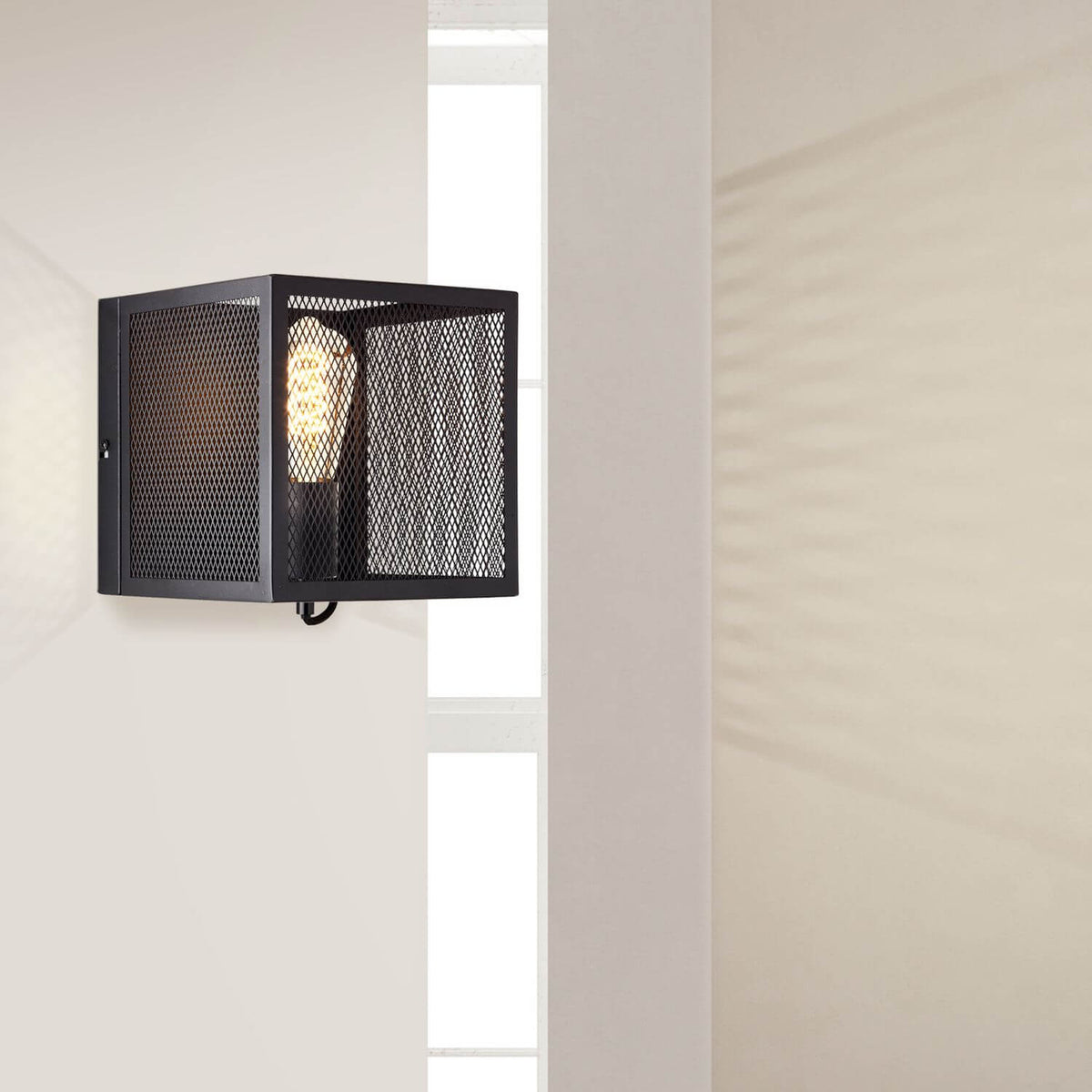 Applique murale noire installée sur cloison blanche, avec fenêtre et ombre portée.
