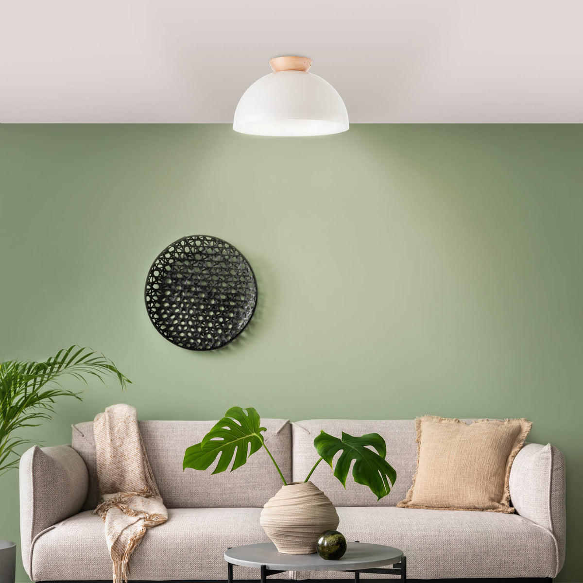 Ambiance salon avec canapé beige, plante verte et plafonnier allumé au-dessus