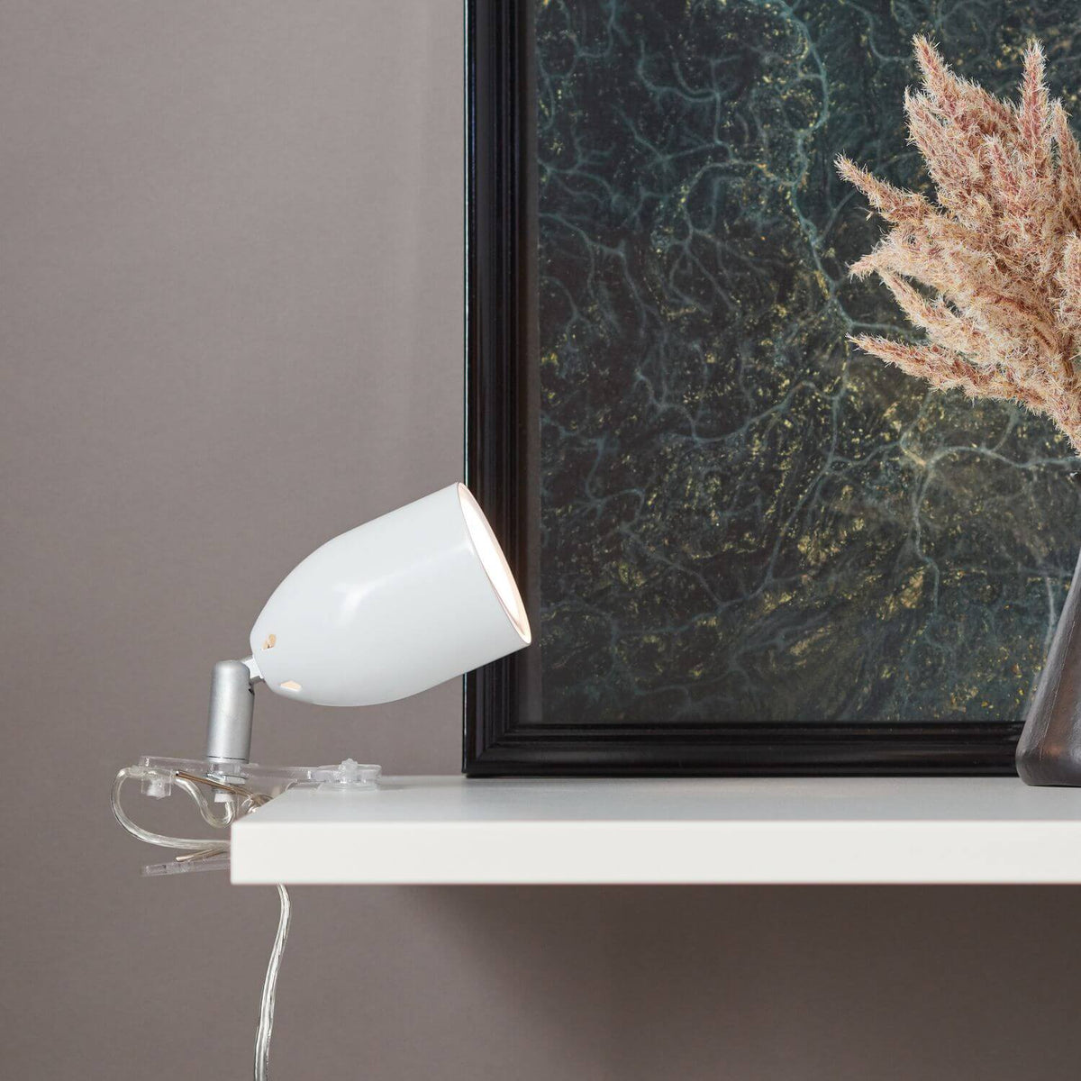 Mise en ambiance de la lampe pincée sur une étagère blanche devant un cadre