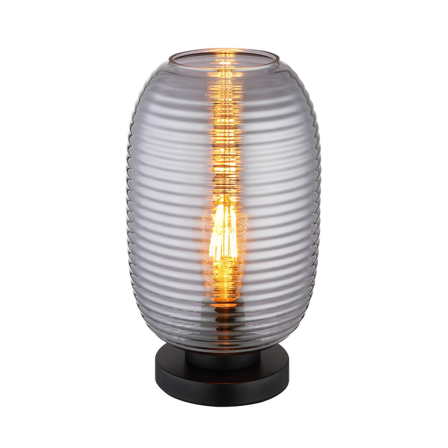 Lampe de table allumée, vue de face sur fond blanc, verre côtelé et base noire.