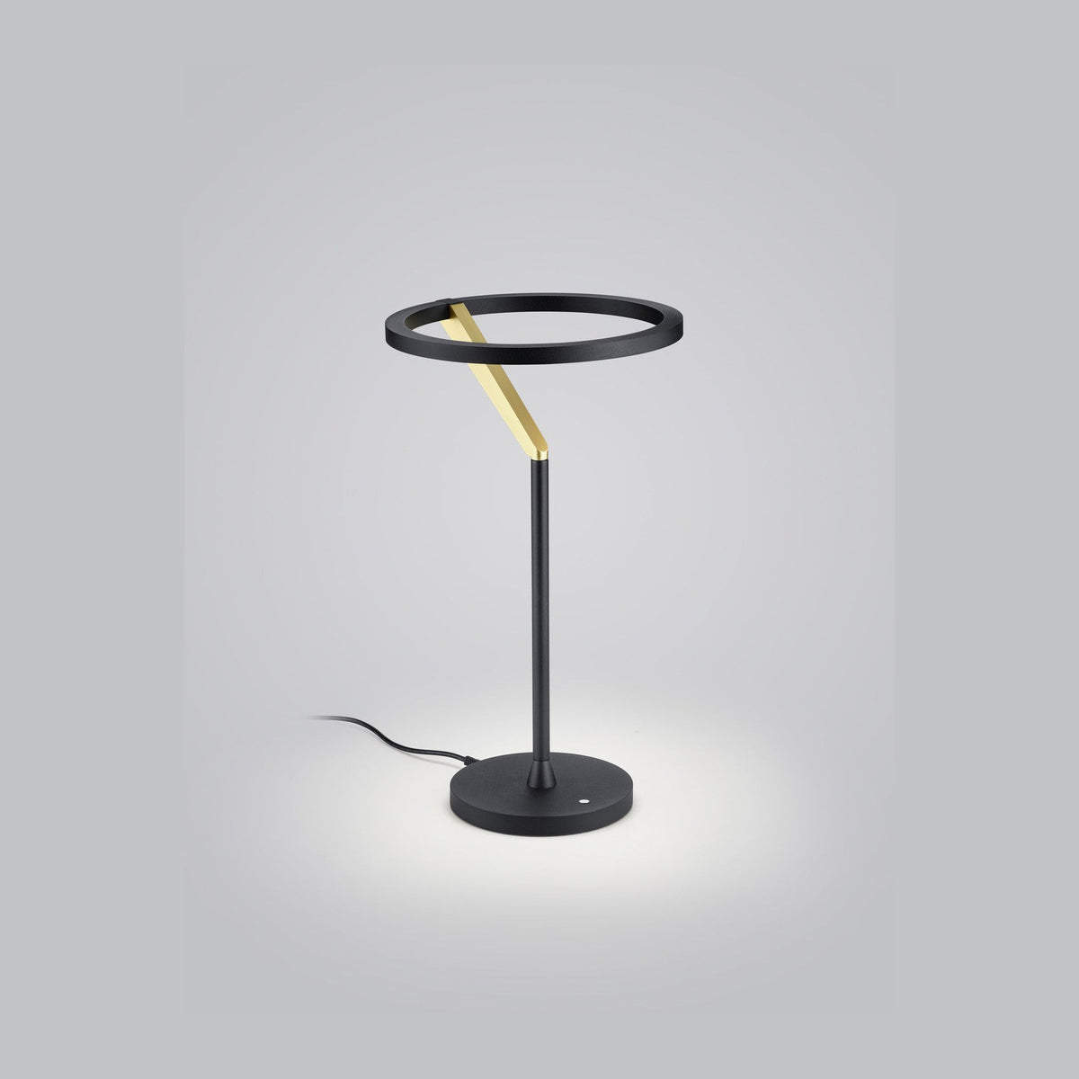 Lampe à poser de face sur fond gris, anneau noir et tige dorée inclinée