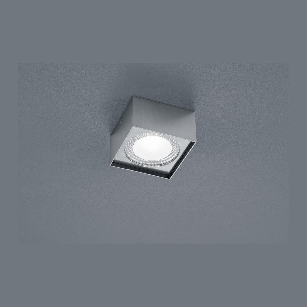 Plafonnier carré nickel vu de face, fixé au plafond gris, verre strié lumineux