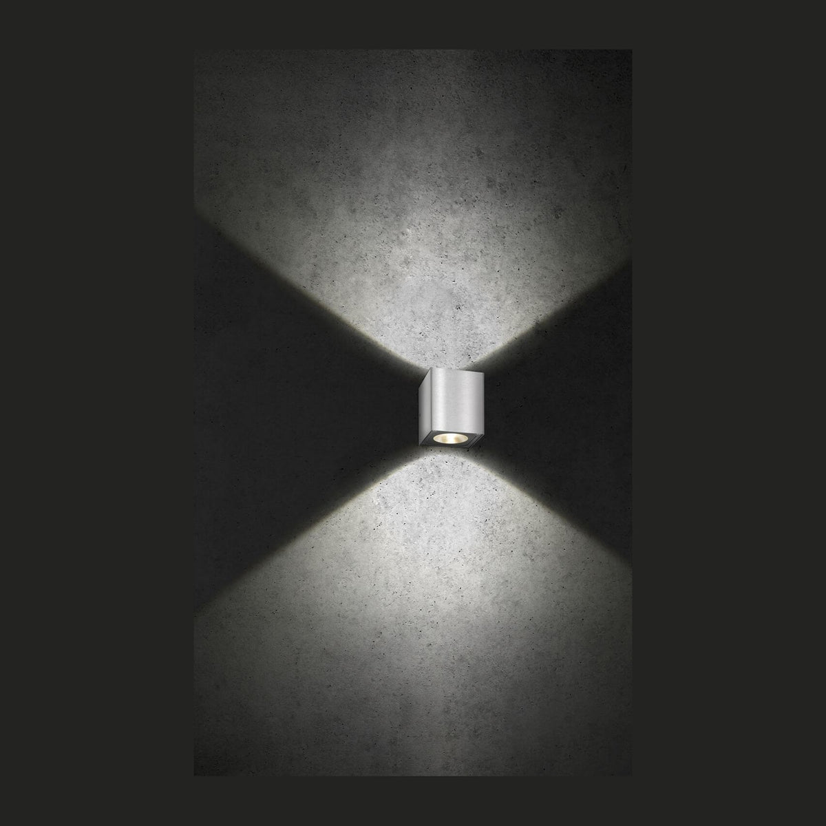 Applique murale cube en inox brossé éclairant un mur béton vers le haut