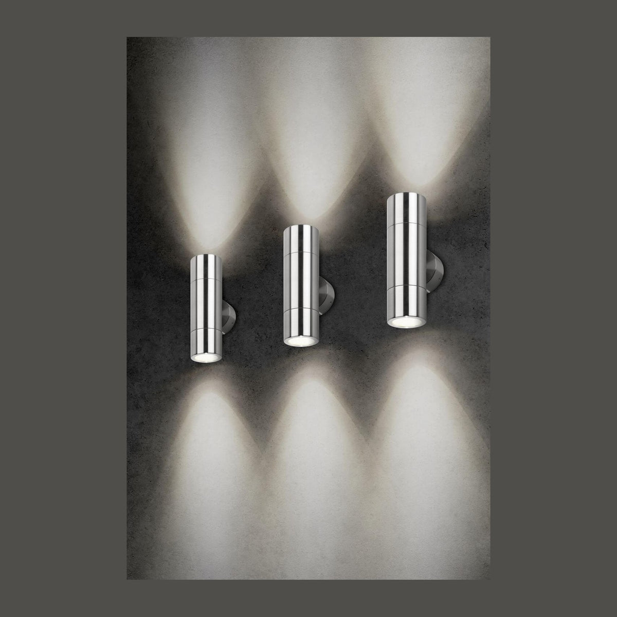 Trois appliques murales en inox éclairant vers le haut et le bas sur fond gris