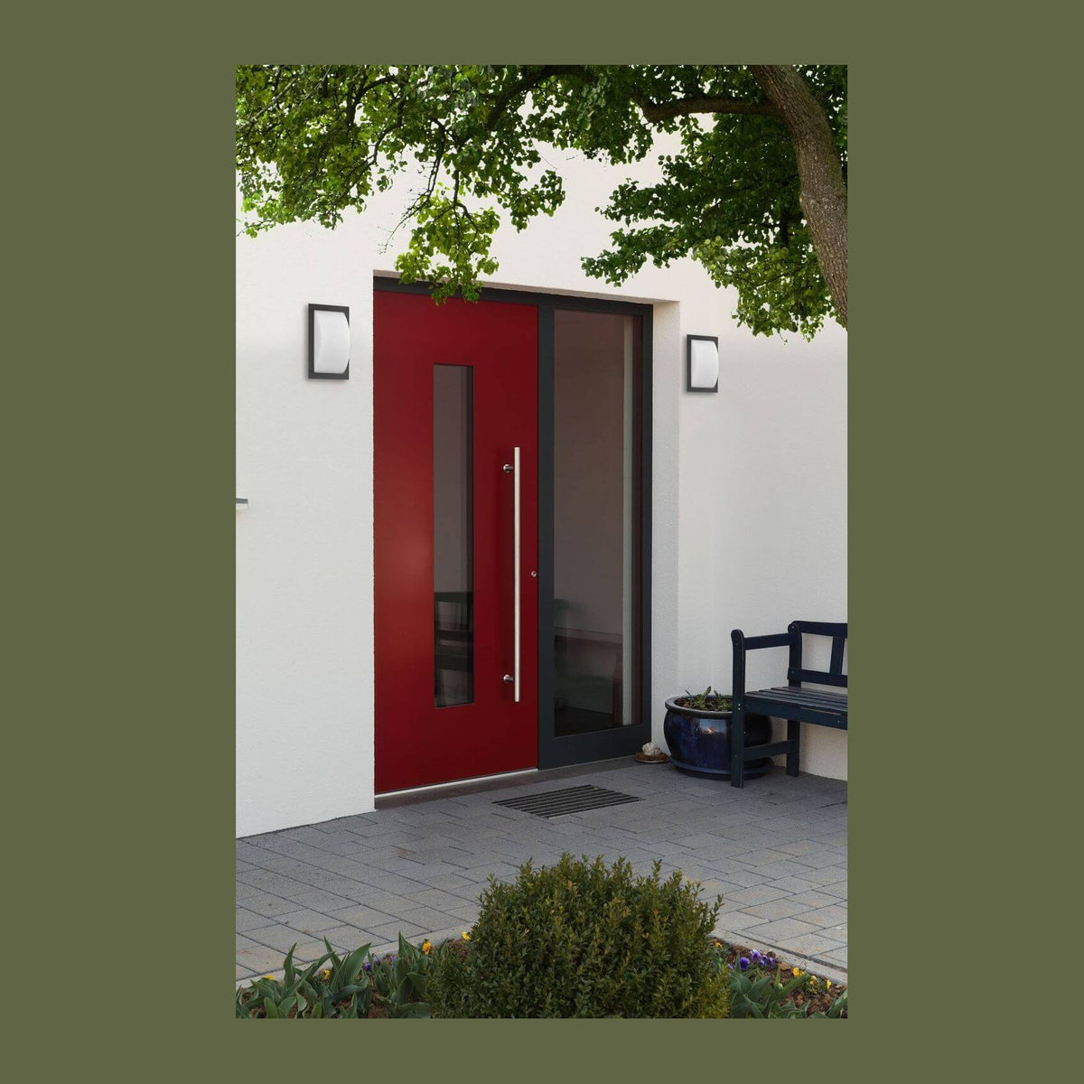 Deux appliques anthracite encadrent une porte d'entrée rouge, mise en ambiance extérieure