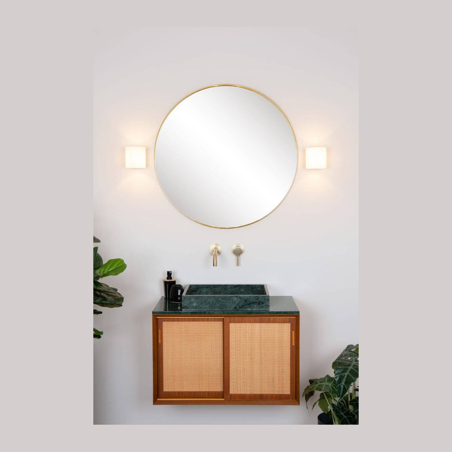 Deux appliques murales opale encadrant un miroir rond dans une salle de bain claire