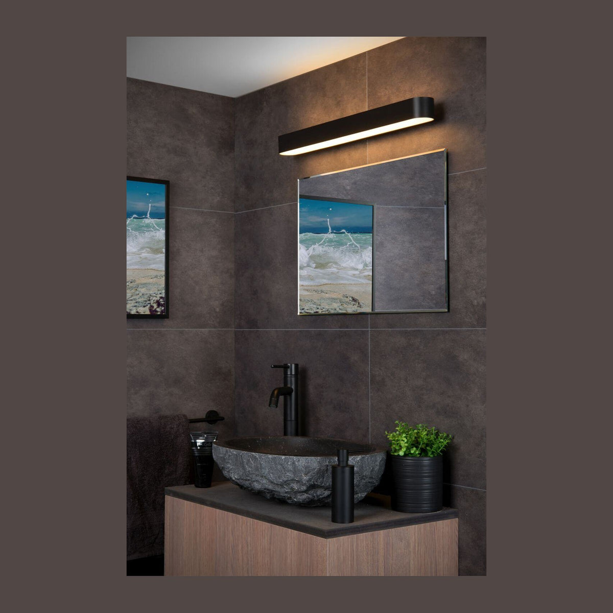Applique murale noire allumée au-dessus d'un miroir dans une salle de bain sombre.