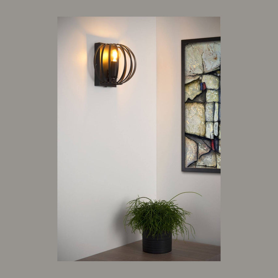 Applique murale noire allumée sur un mur blanc, près d'un tableau et d'une plante