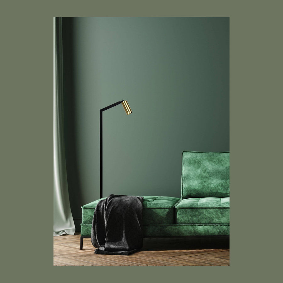 Lampadaire noir à tête dorée dans un salon vert, canapé velours et plaid