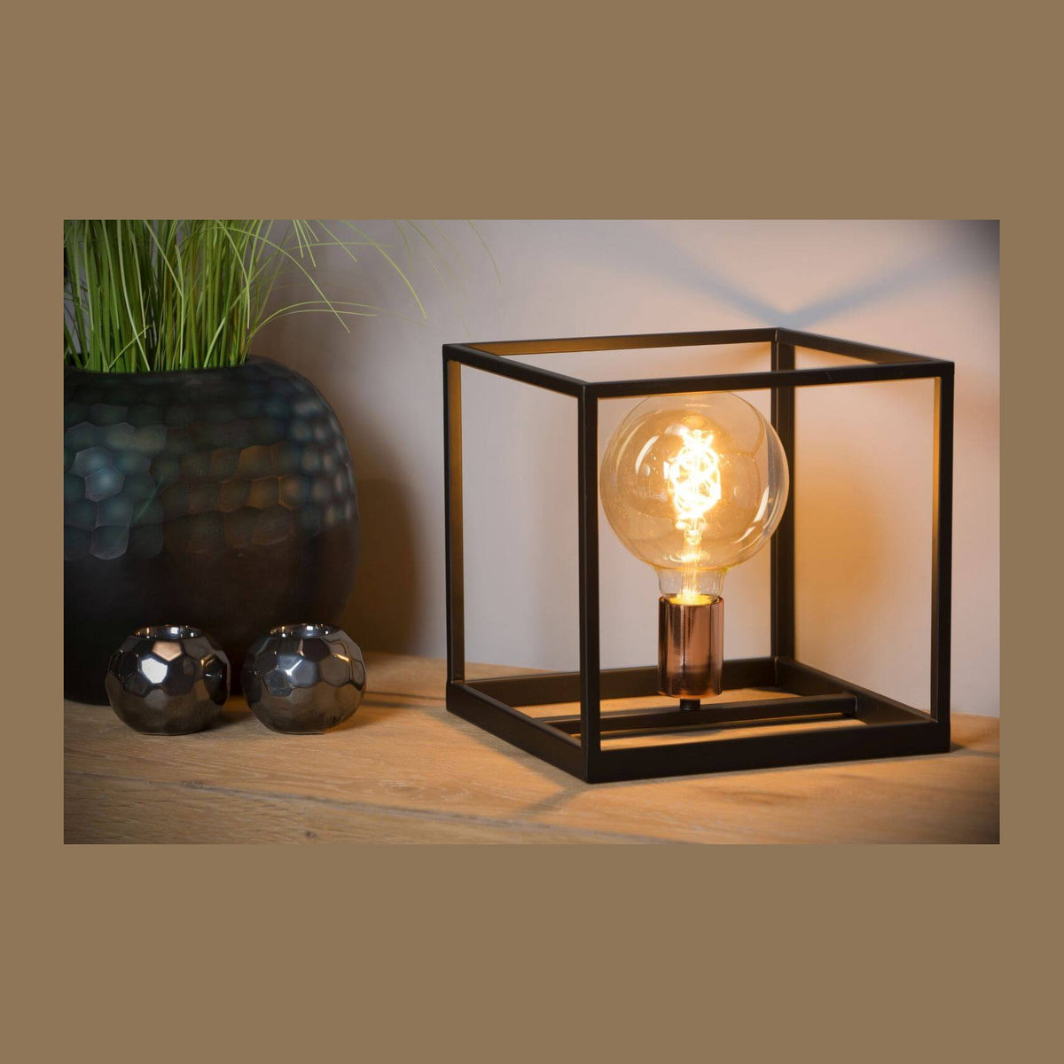 Lampe cube noire posée sur un meuble en bois, ambiance chaleureuse avec plante