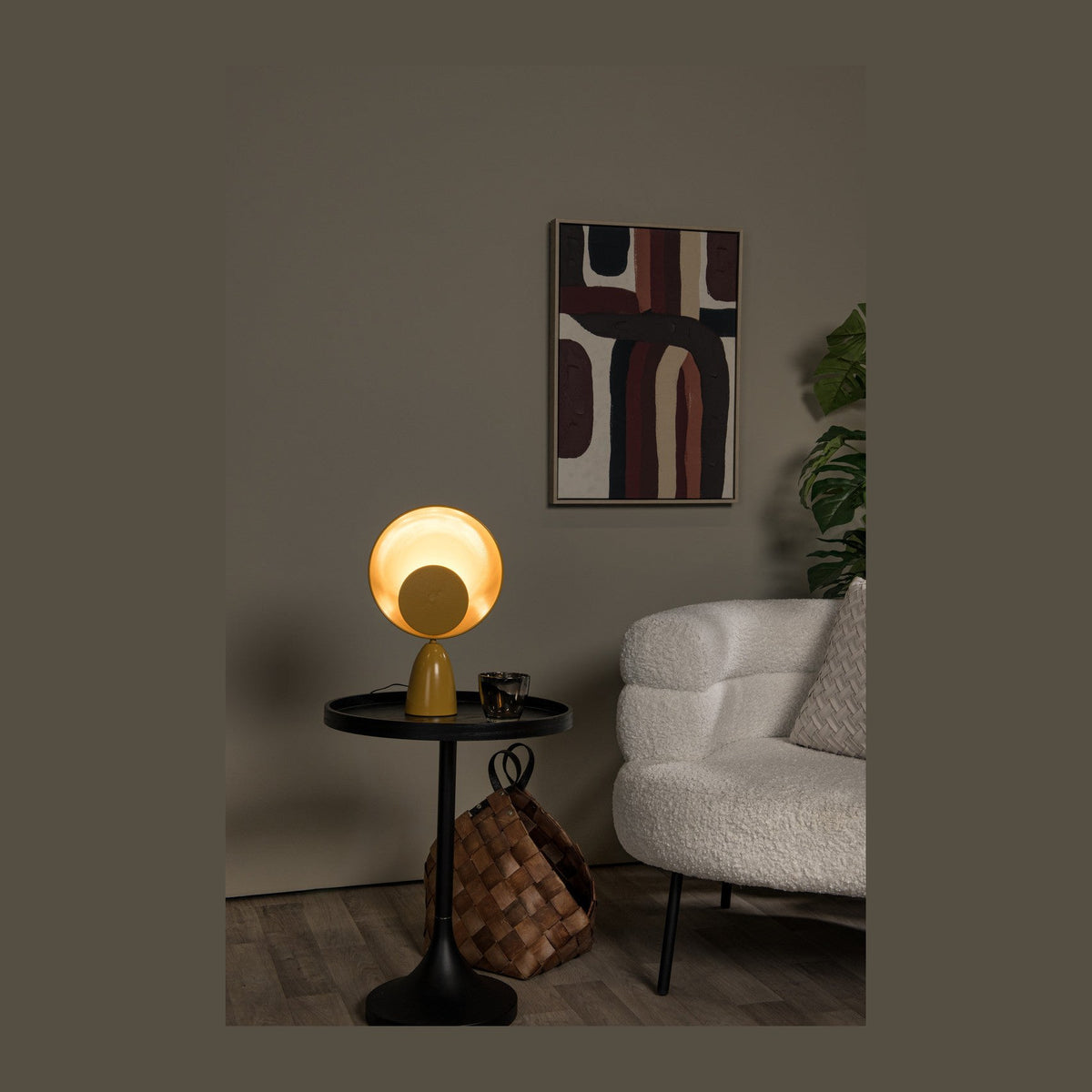 Lampe jaune allumée posée sur table d'appoint noire, canapé blanc et tableau abstrait