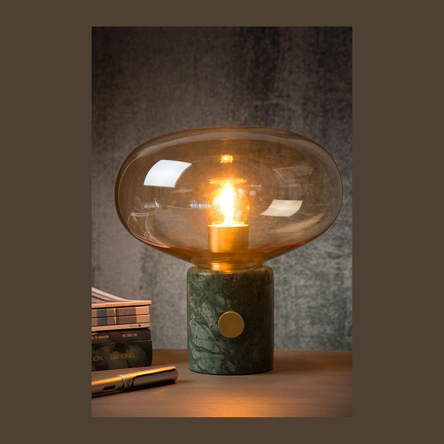 Lampe à poser allumée sur une table en bois, fond gris, livres et stylo.