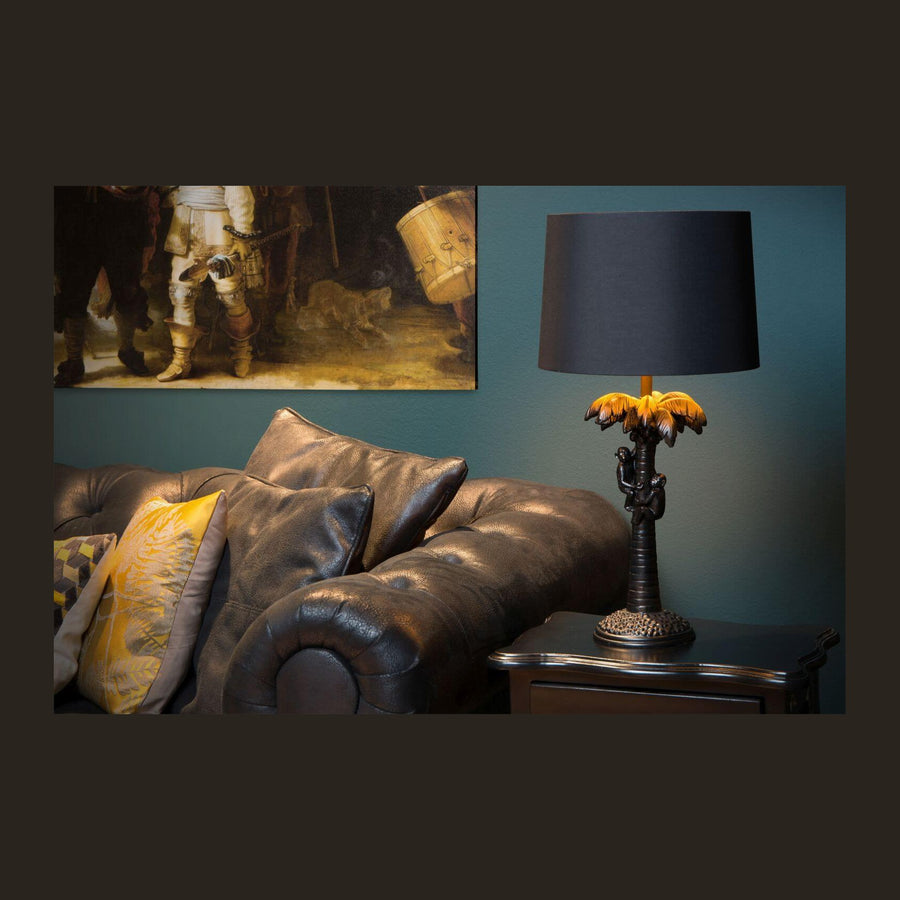 Lampe à poser sur un chevet en bois sombre, canapé en cuir et tableau en fond