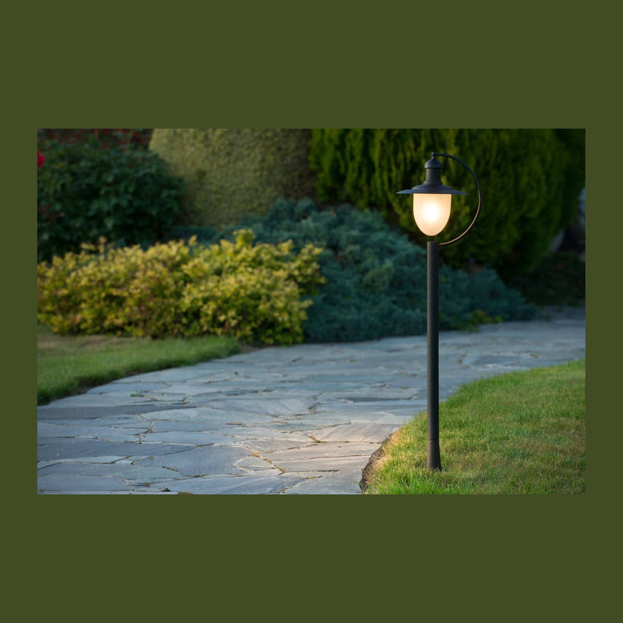 Lampadaire noir allumé au bord d'une allée en pierre dans un jardin.