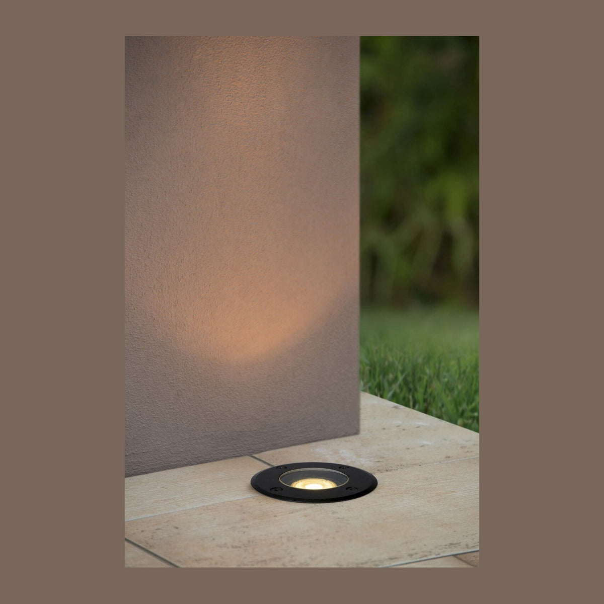 Luminaire encastré au sol éclairant un mur extérieur, terrasse en pierre et pelouse