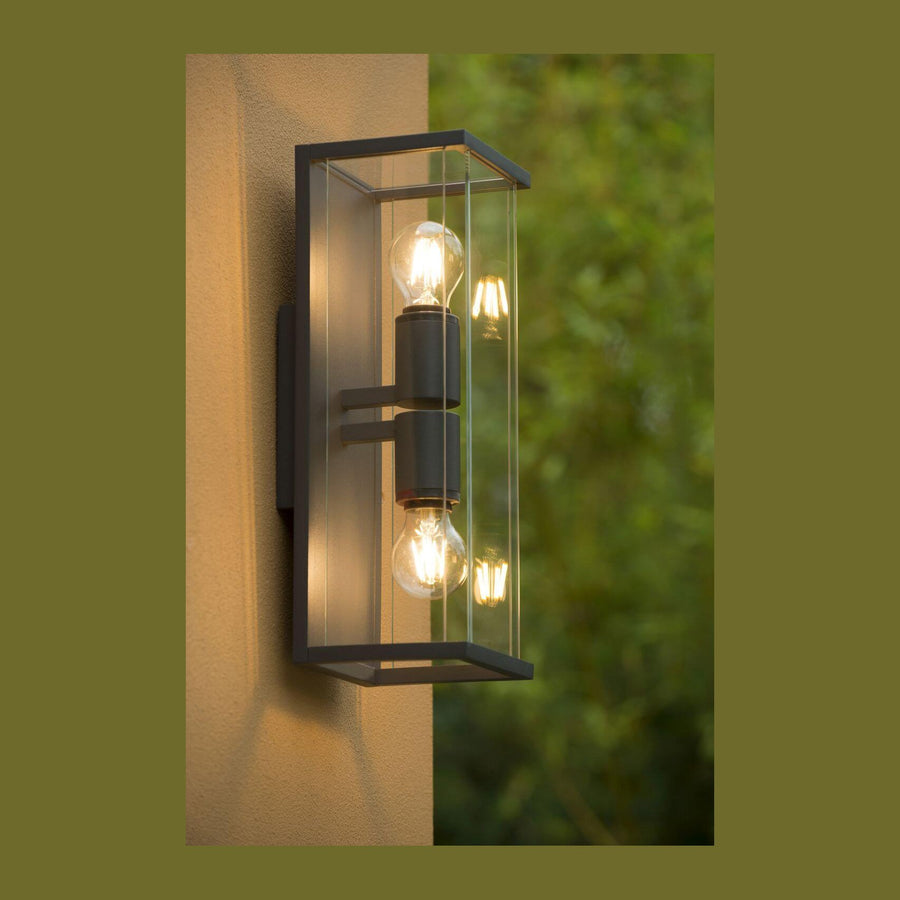 Applique anthracite à deux ampoules allumées fixée sur un mur beige extérieur.