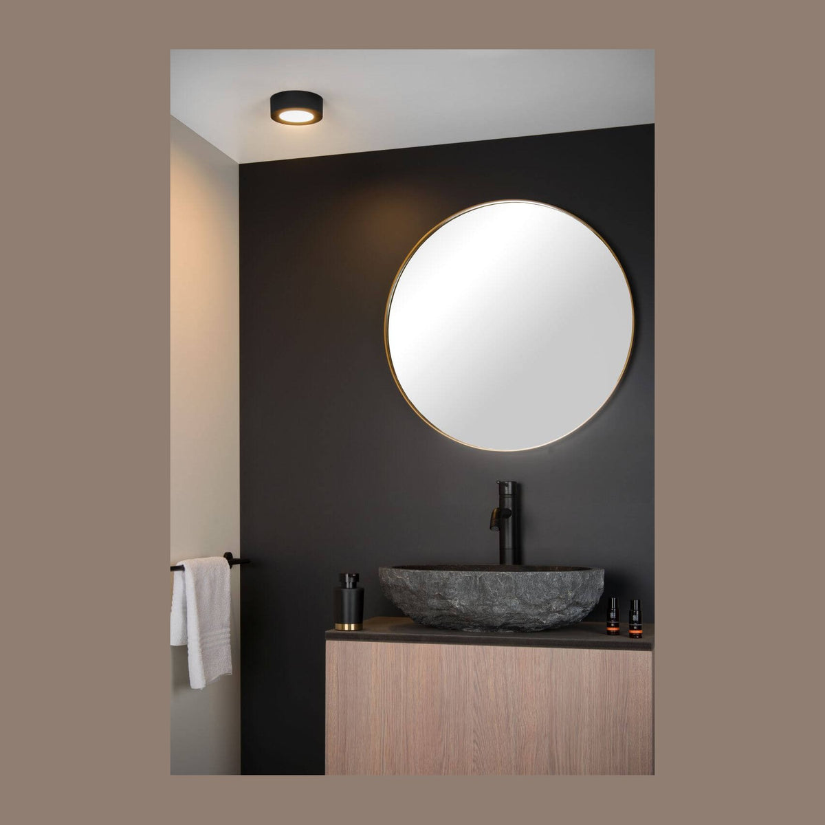 Vue d'ambiance d'une salle de bain sombre avec plafonnier rond noir allumé au plafond.