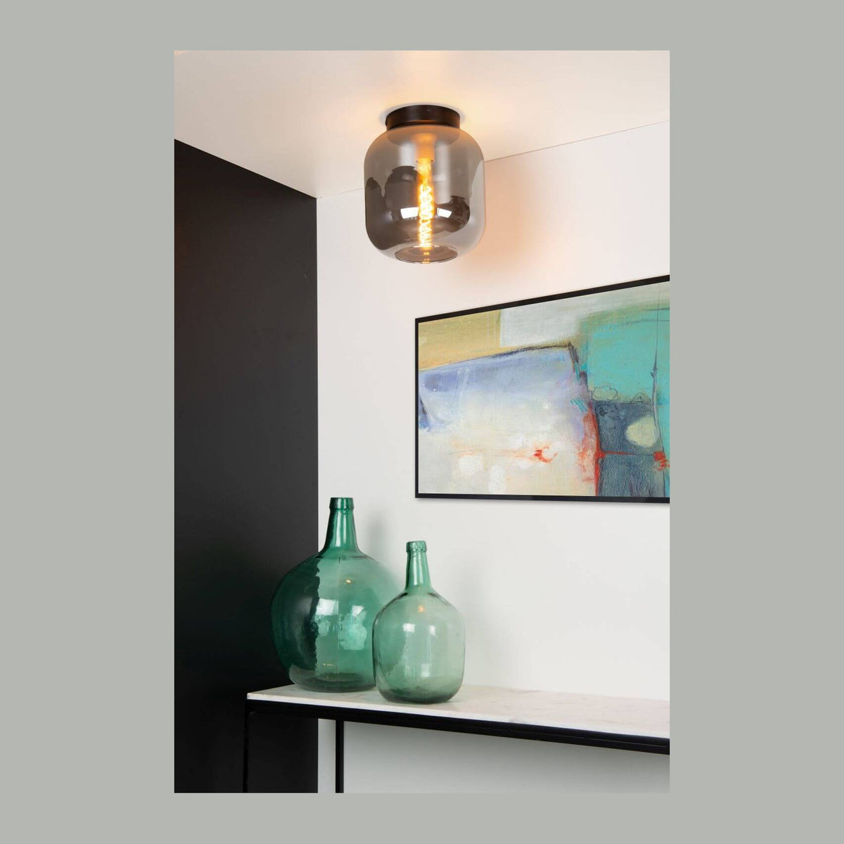Plafonnier en verre fumé allumé au plafond au-dessus d'un tableau et de bouteilles vertes.