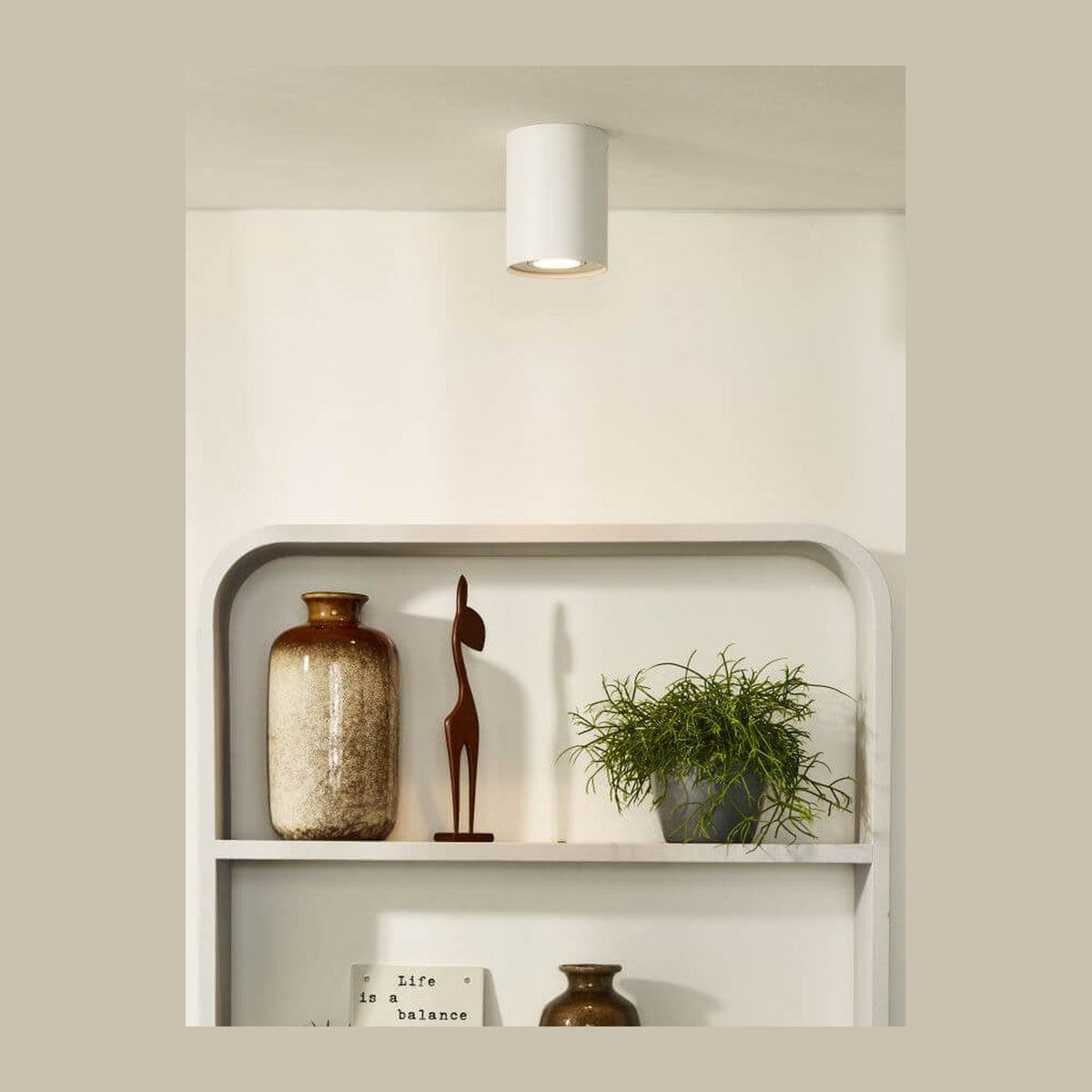 Plafonnier cylindrique blanc fixé au plafond au-dessus d'une étagère avec objets décoratifs.