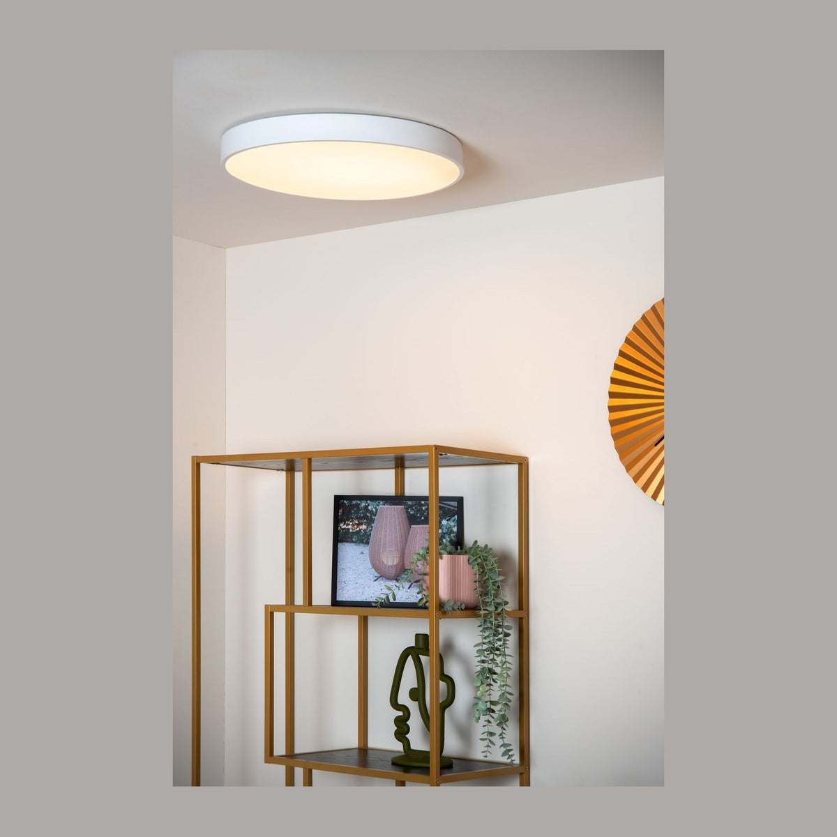 Plafonnier rond blanc allumé au plafond dans un intérieur avec étagère dorée