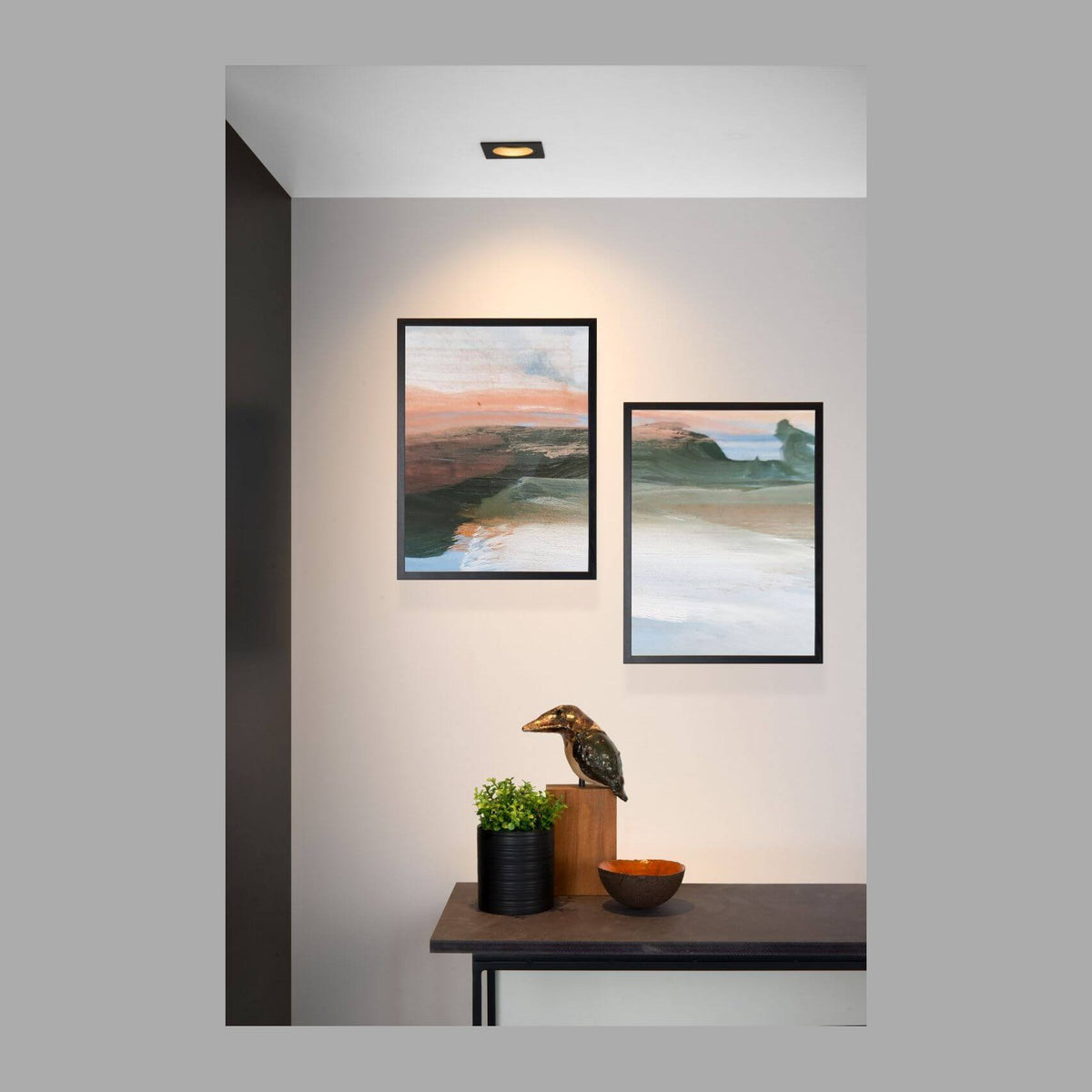 Spot encastré noir au plafond éclairant une scène murale avec deux tableaux et une console déco.
