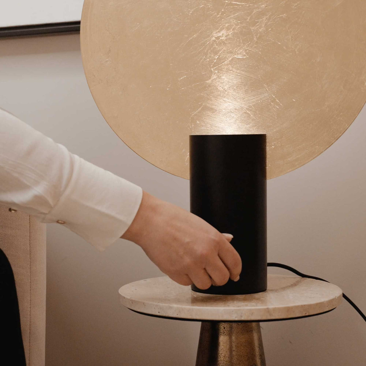 Main actionnant le socle de la lampe sur une table ronde en marbre.