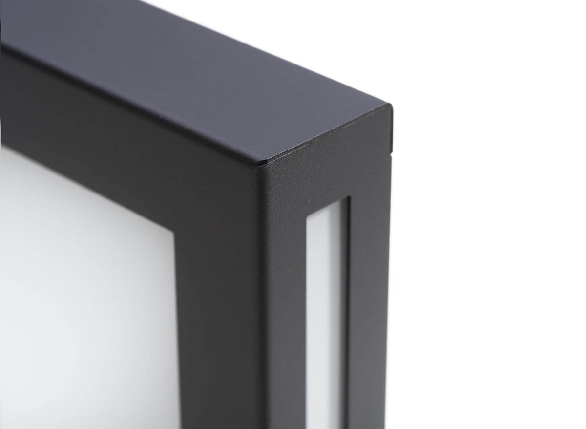 Détail du coin supérieur de l'applique extérieure anthracite avec finition grainée et diffuseur blanc.
