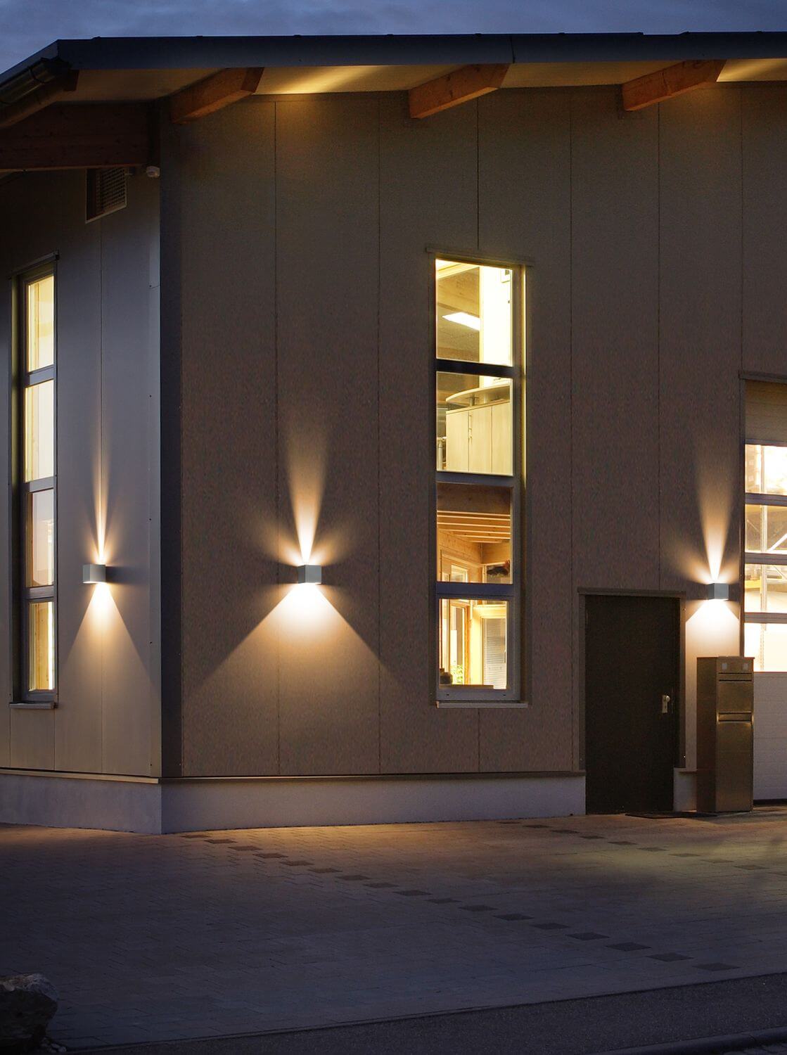 Quatre appliques éclairant la façade boisée d'une maison au crépuscule