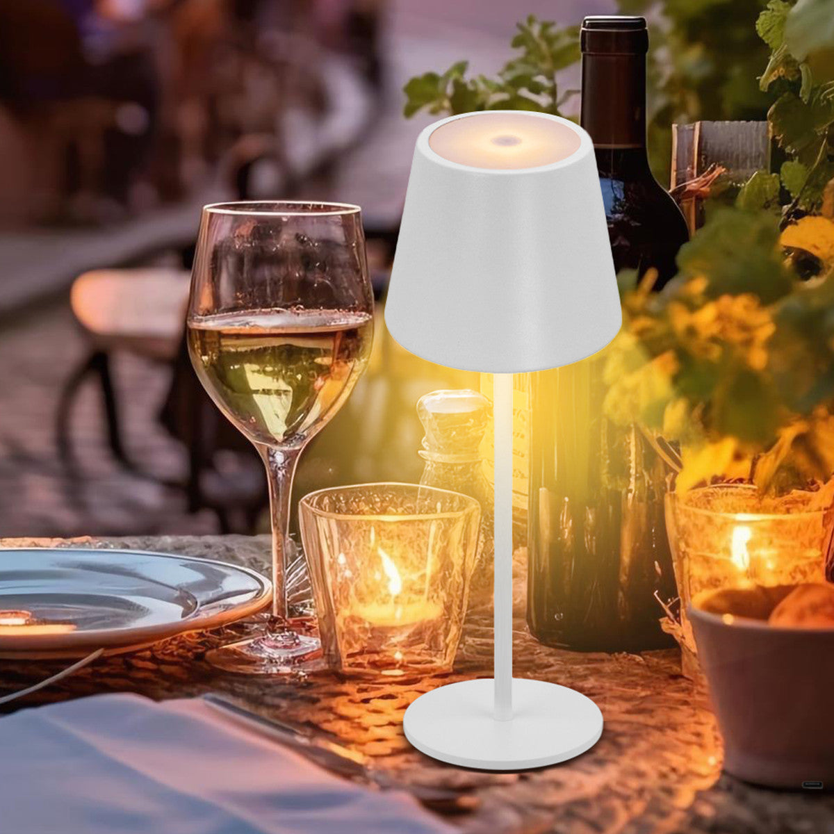 Lampe blanche allumée sur une table de jardin, près d'un verre de vin blanc