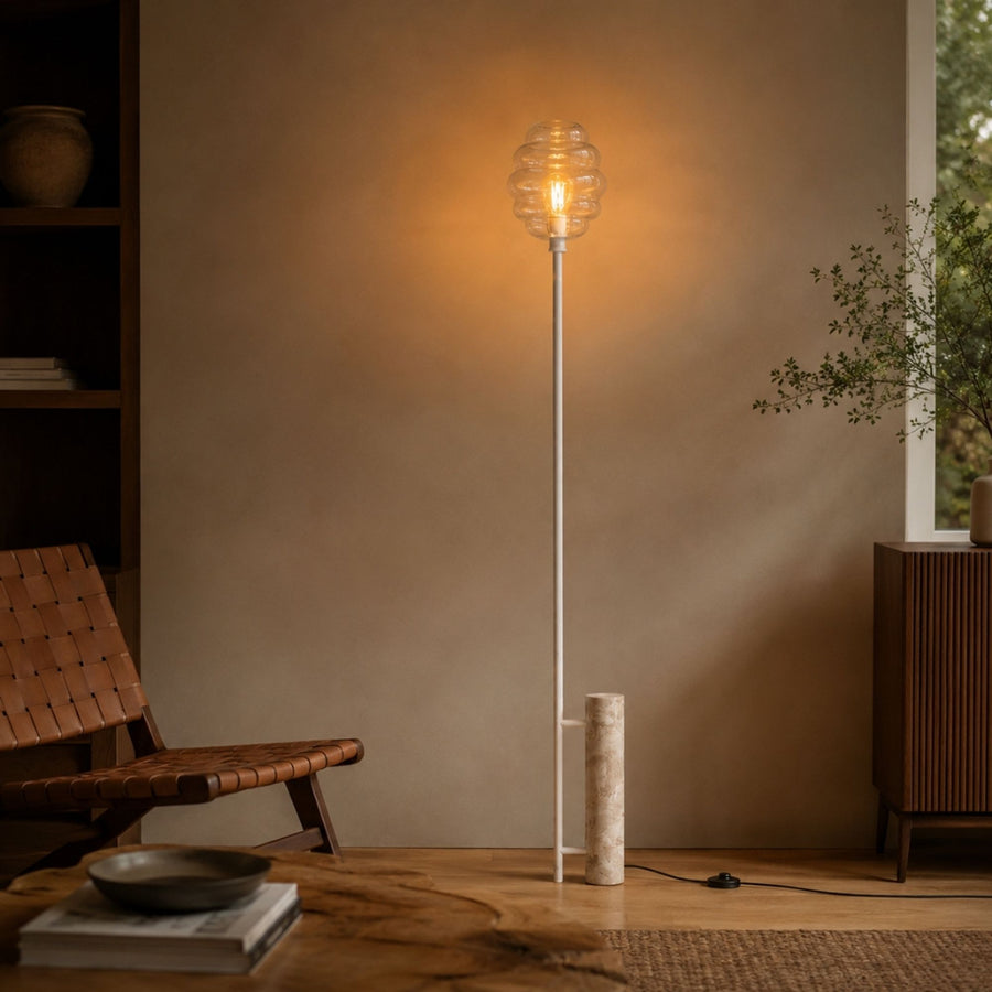Intérieur avec fauteuil en cuir tressé et lampadaire allumé contre le mur beige.