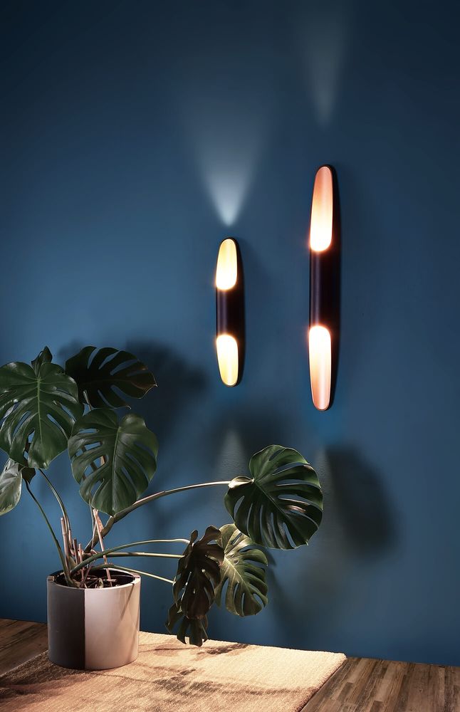 Mise en ambiance sur mur bleu avec deux appliques allumées et plante verte.