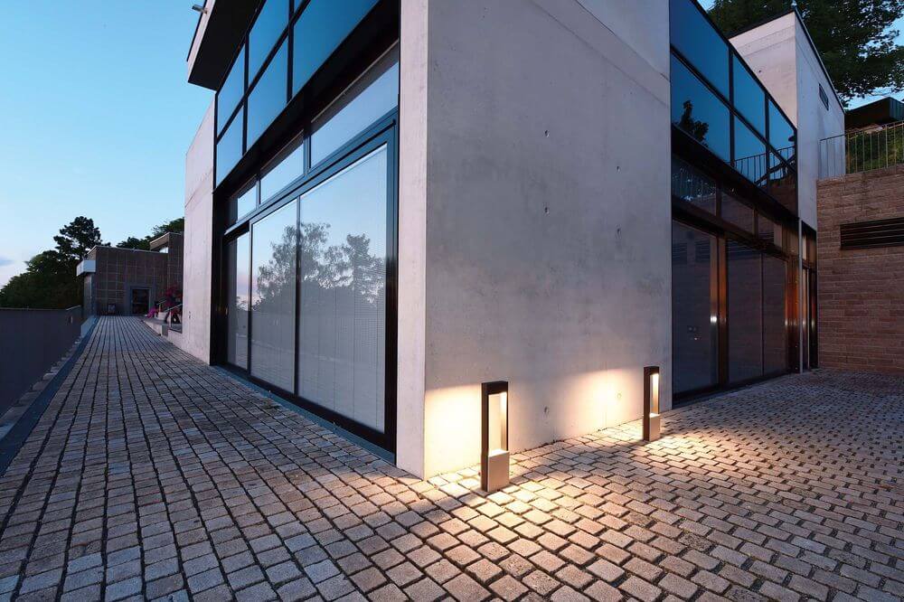Mise en ambiance nocturne, deux lampadaires éclairant une allée pavée devant une maison